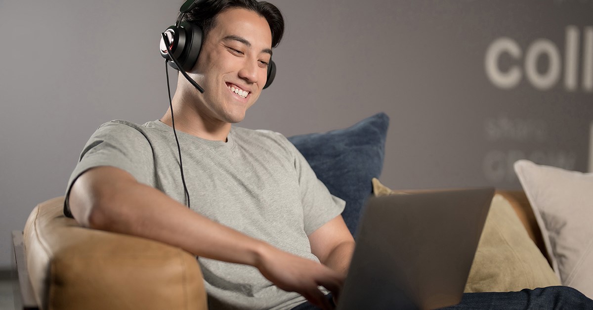 Young man is sitting in front of a laptop wearing a Kensington H2000 headset.