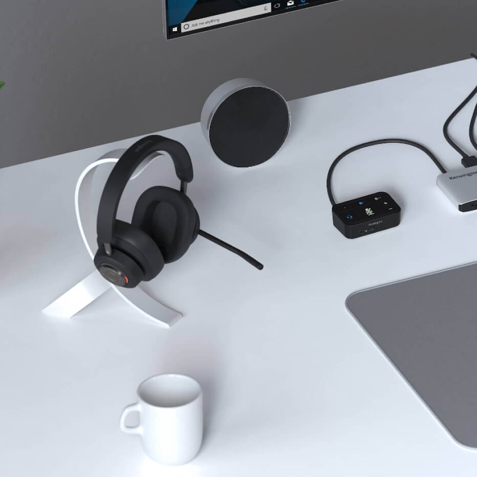 Närbild på Kensington H3000 Bluetooth Over-ear-headset och Universal 3-i-1 Pro Headsetljudomkopplare som en del av en professionell skrivbordskonfiguration