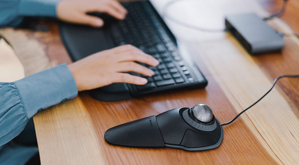 Mouse Trackball Orbit de Kensington y persona tipeando en el teclado de fondo