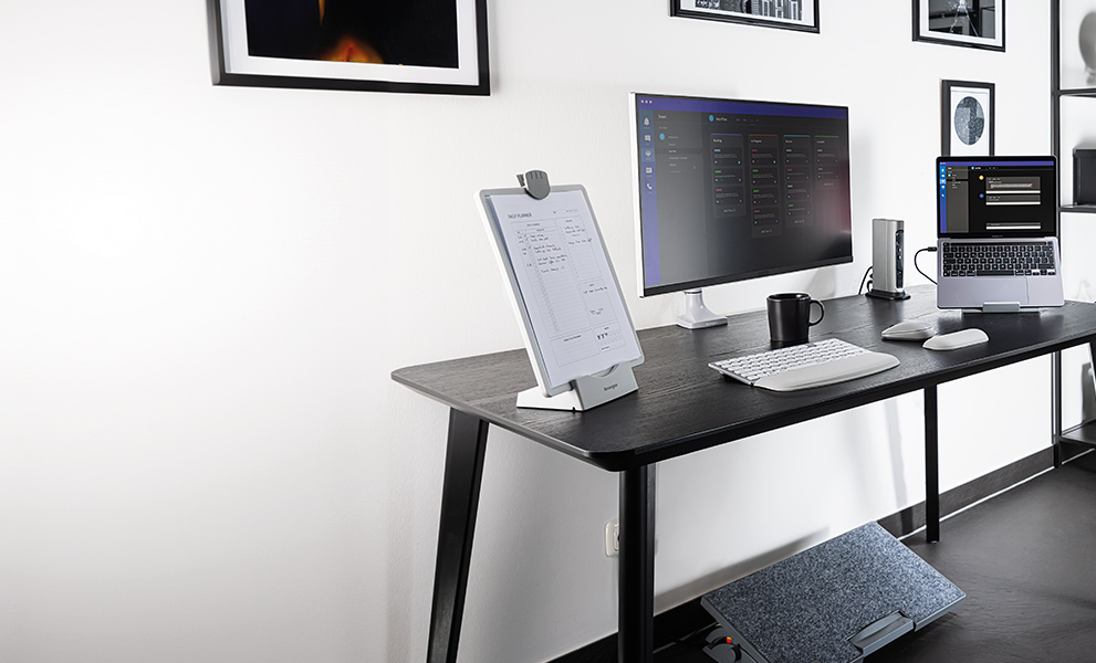 Configuración ergonómica de escritorio de una oficina en casa con teclado, ratón, brazo para monitor y reposapiés de Kensington.
