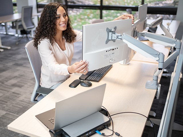 person adjusting dual monitor arm at desk