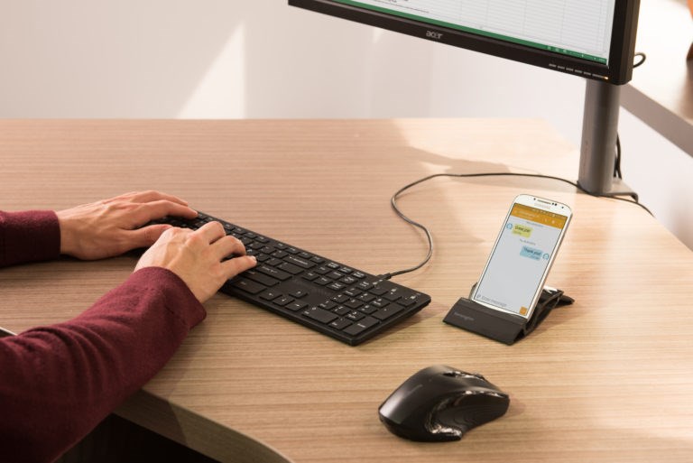 Person typing on a keyboard and looking at a cellphone 