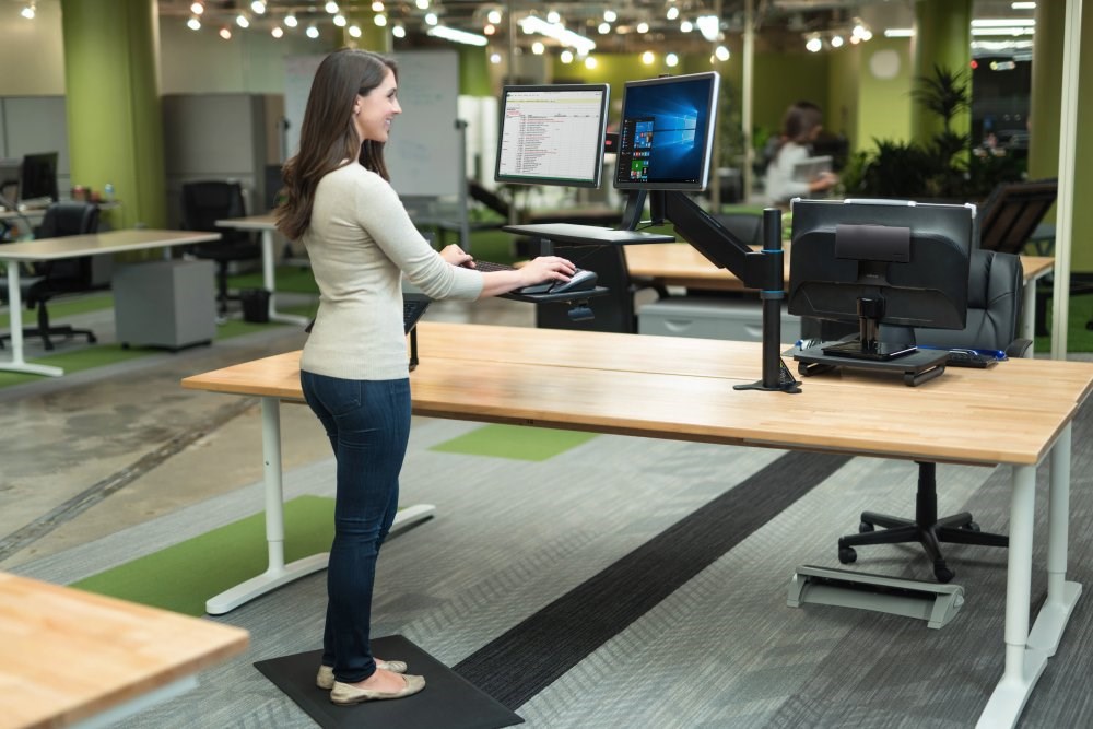 Woman standing on an anti-fatigue mat and working at a dual monitor setup with a monitor arm