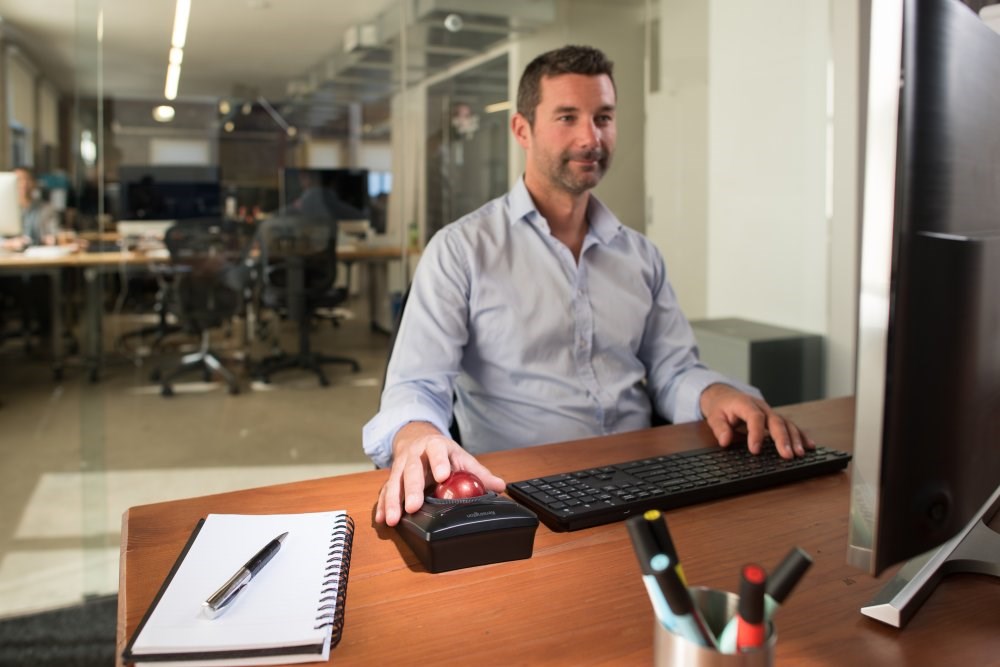 A man working on a desktop computer and using a Kensington Expert Mouse® Wireless Trackball