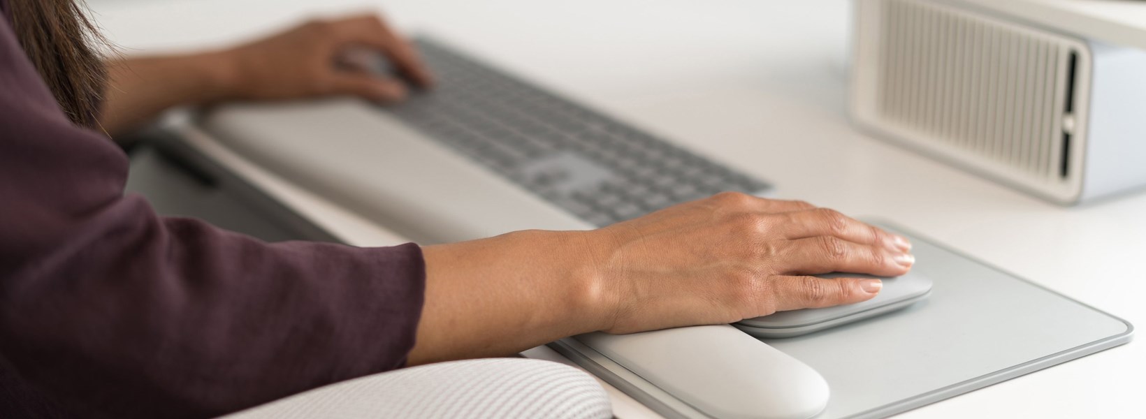 Woman typing on a keyboard and using a mouse paired with a wrist rest