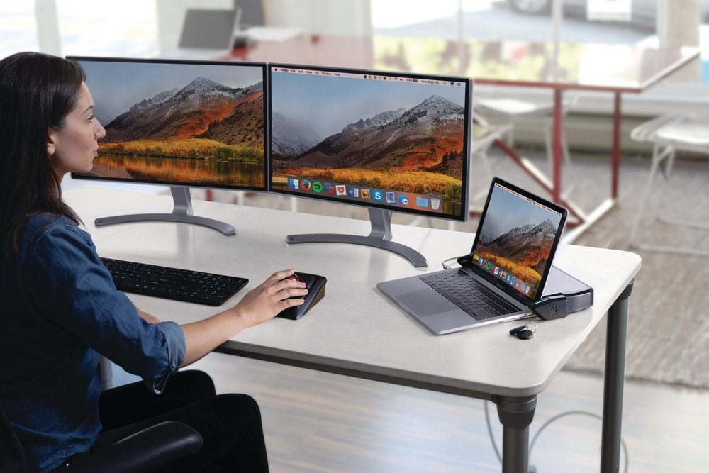 Woman working on a dual monitor setup with a laptop connected to a locking dock station