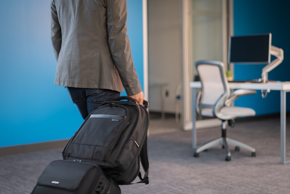 A man walking with a suitcase and a Kensington laptop backpack attached to the suitcase handle