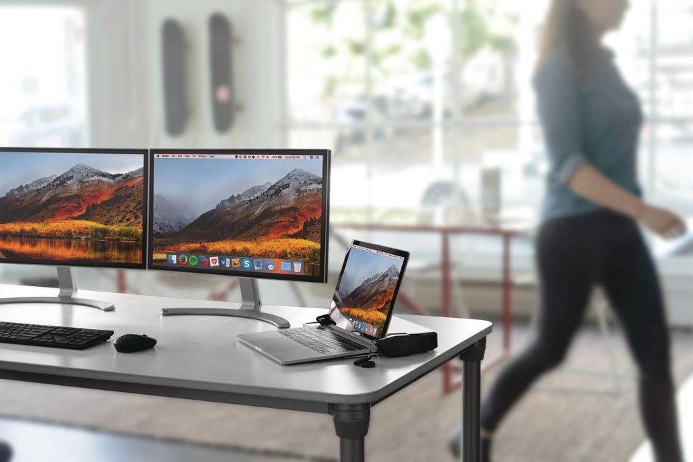 Woman walking past a desk with a laptop connected to a DisplayLink docking station