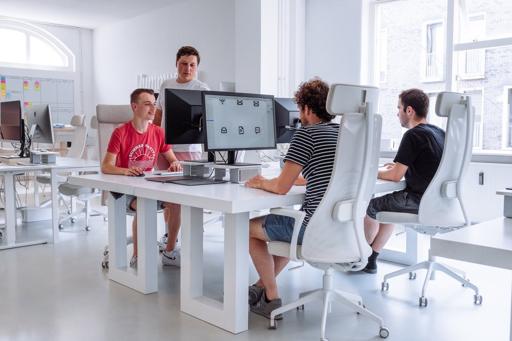 Teenagers working at computer desk stations while an adult watches