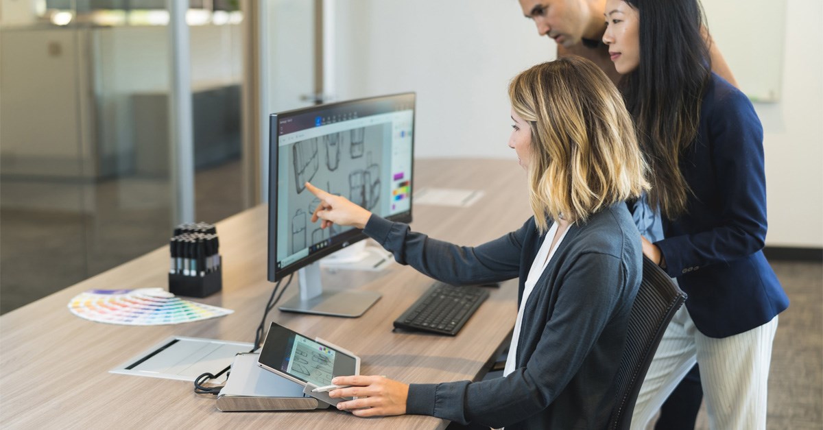 Three employees talking and looking at a monitor while one works on a tablet