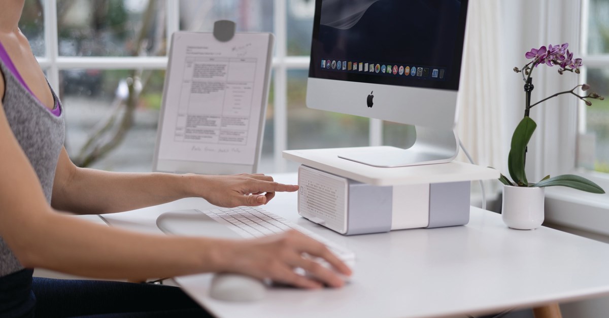 Person working at an iMac with a Kensington CoolView™ Wellness Monitor Stand with Desk Fan