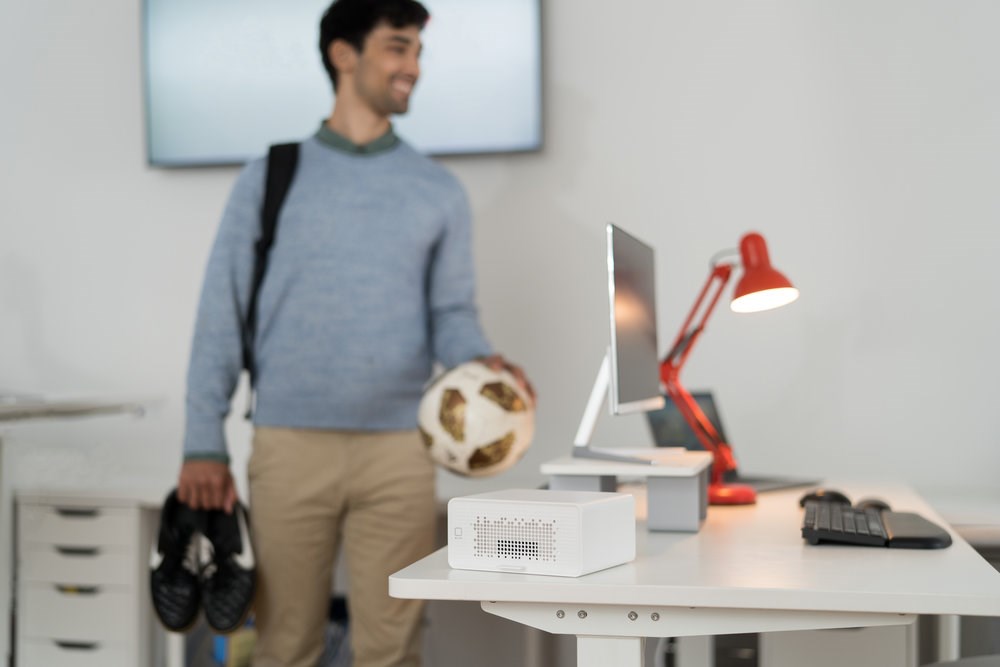Man walking past a desk with a desktop monitor and a Kensington air purifier