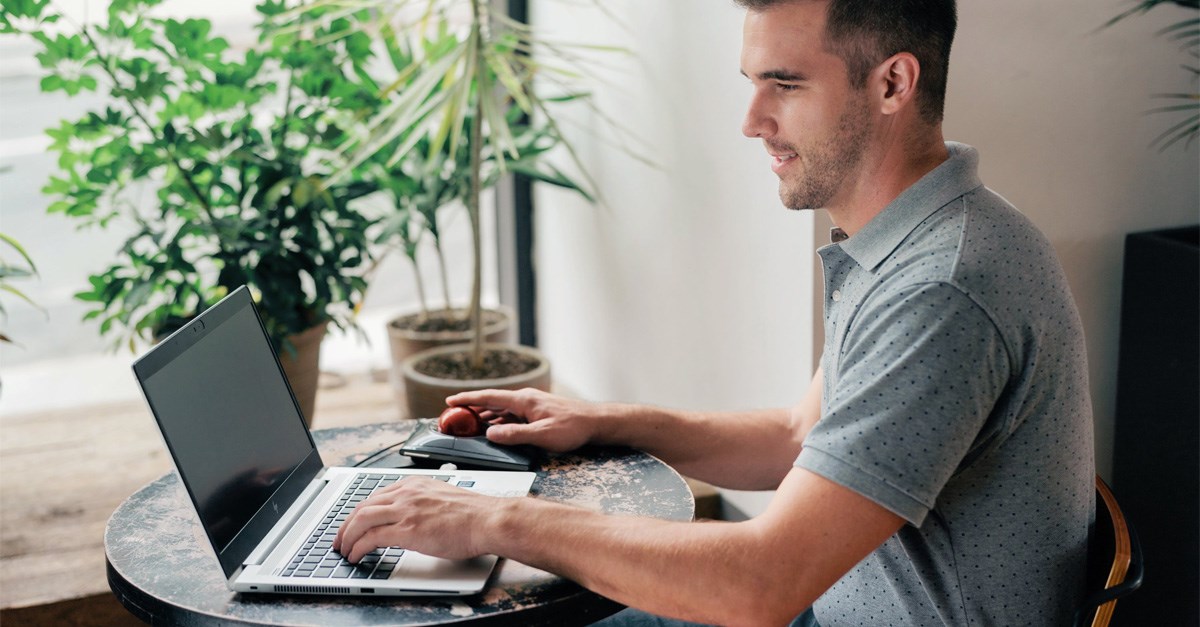 Man working on a laptop with a Kensington trackball mouse