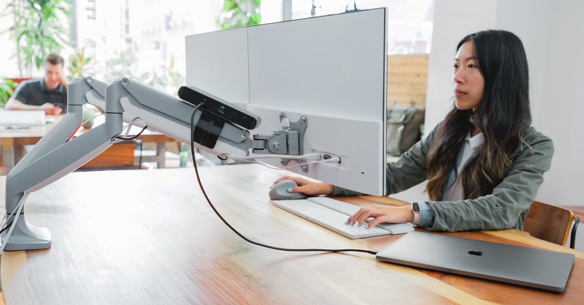 A woman working at a monitor connected to a monitor arm and a docking station