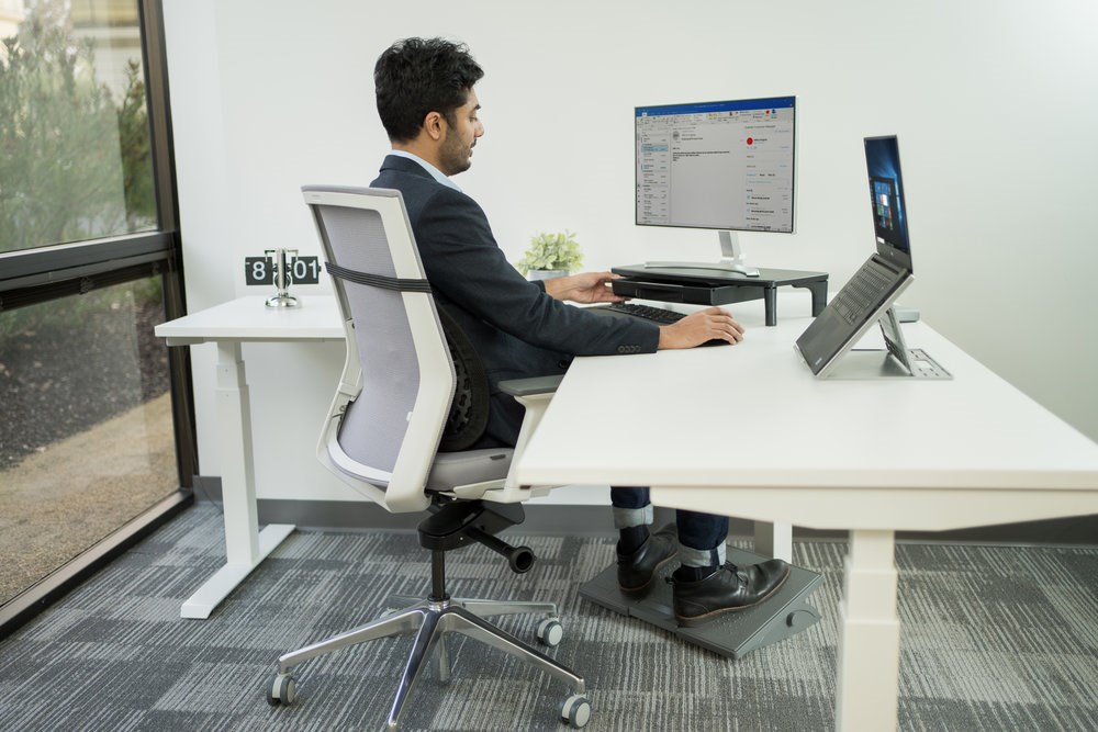 Man working at a desk with a monitor on a riser and a laptop on a riser