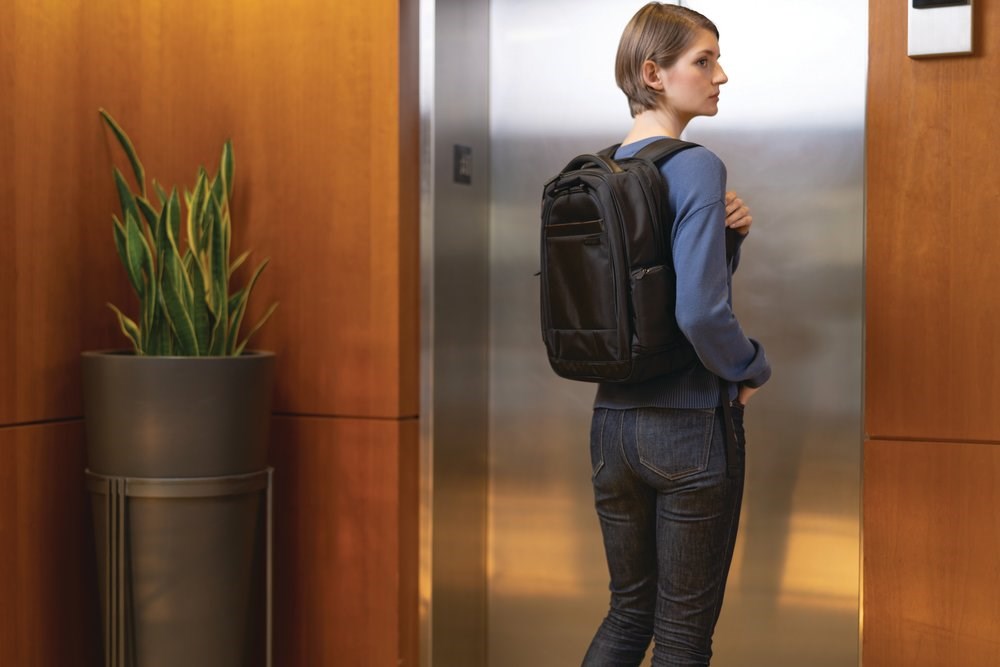Woman waiting for an elevator and wearing a Kensington laptop backpack