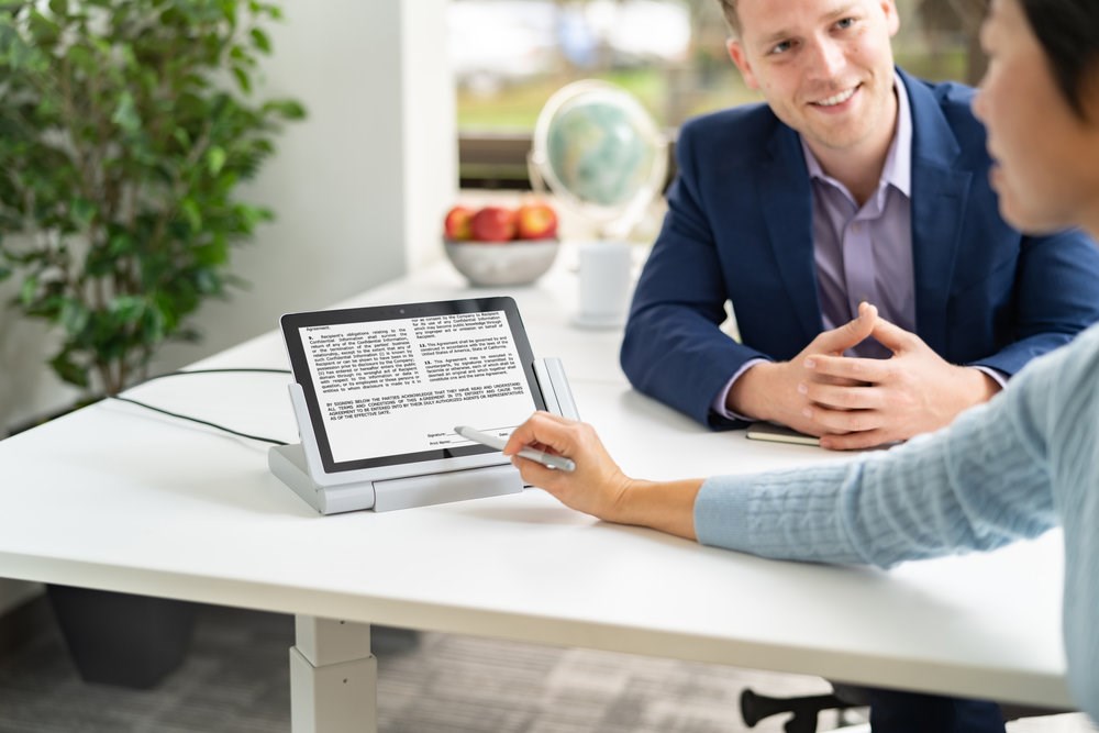 Two people talking while one works on a Microsoft Surface tablet