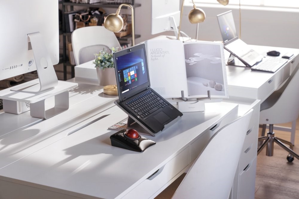 Laptop set up in an office with a Kensington laptop riser, a trackball mouse, and a book stand