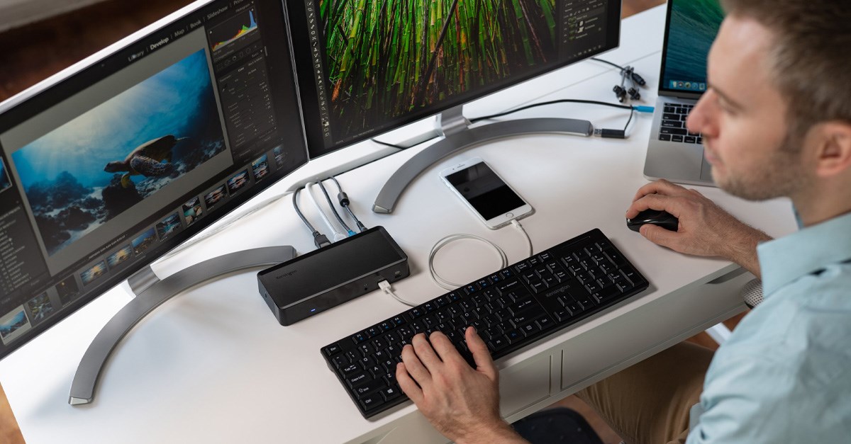 Man working at a dual monitor setup and charging his phone with a docking station 