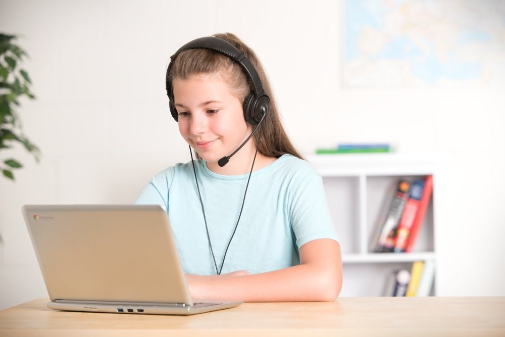 Child wearing a headset with a microphone and looking at a laptop screen