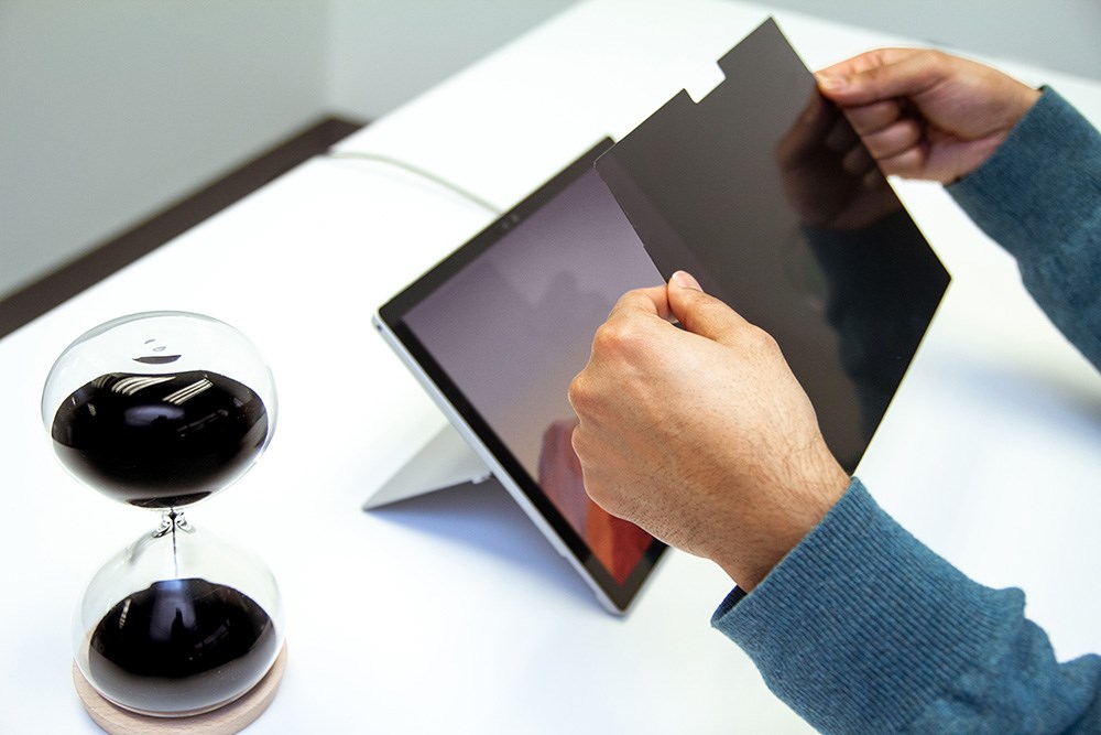 Person placing a privacy screen onto a Microsoft Surface tablet with an hourglass next to it