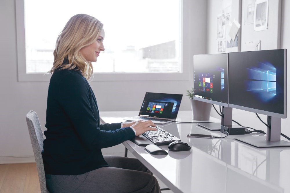 Woman working at a desk with dual monitors and a laptop