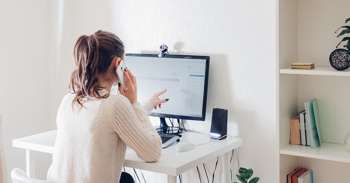 Woman on a phone call and pointing at a desktop computer screen in a home office