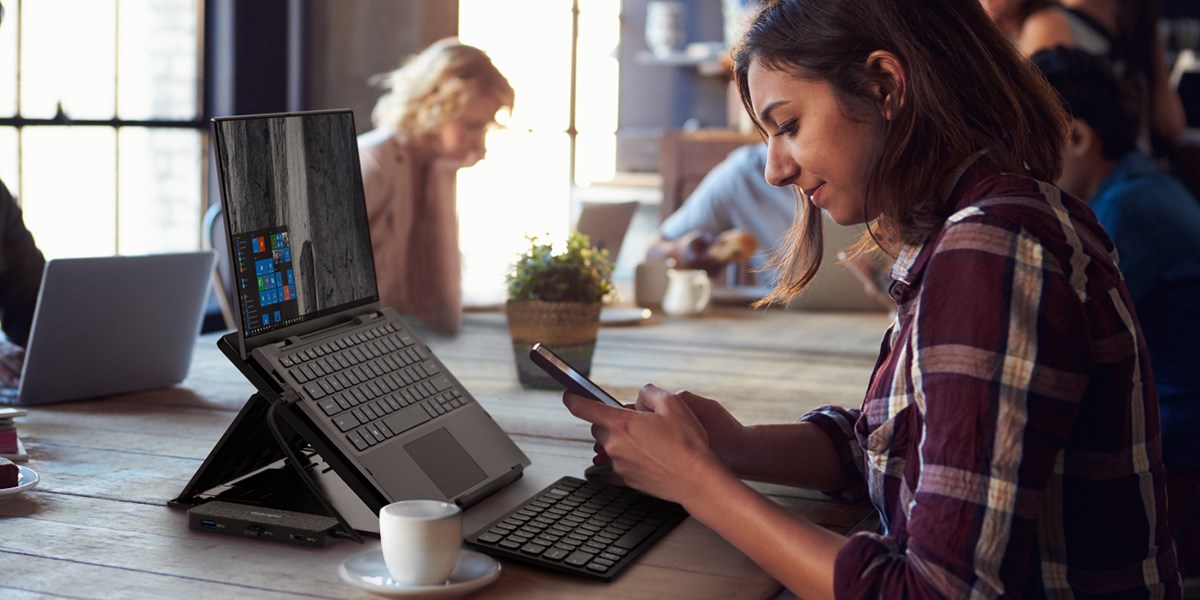 Remote worker in a coffee shop using a Kensington docking station and laptop riser