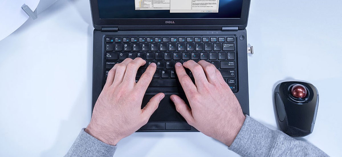 Male's hand working on a laptop with Biometric authentication and a Kensington trackball.