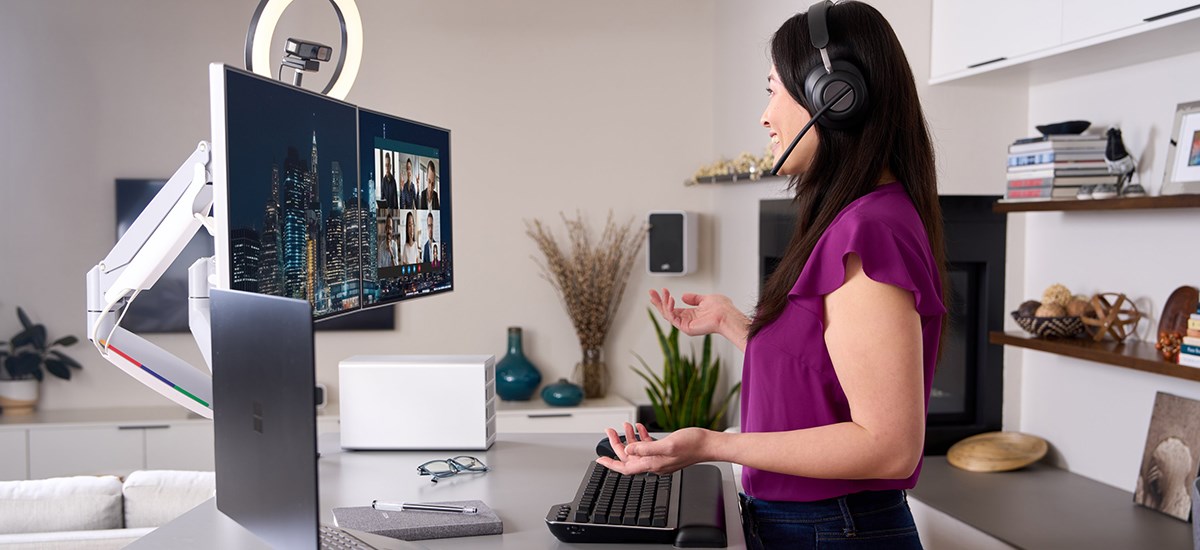 Woman video conferencing with Kensington equipment, using MK7500F QuietType™ Mechanical Keyboard on desk.