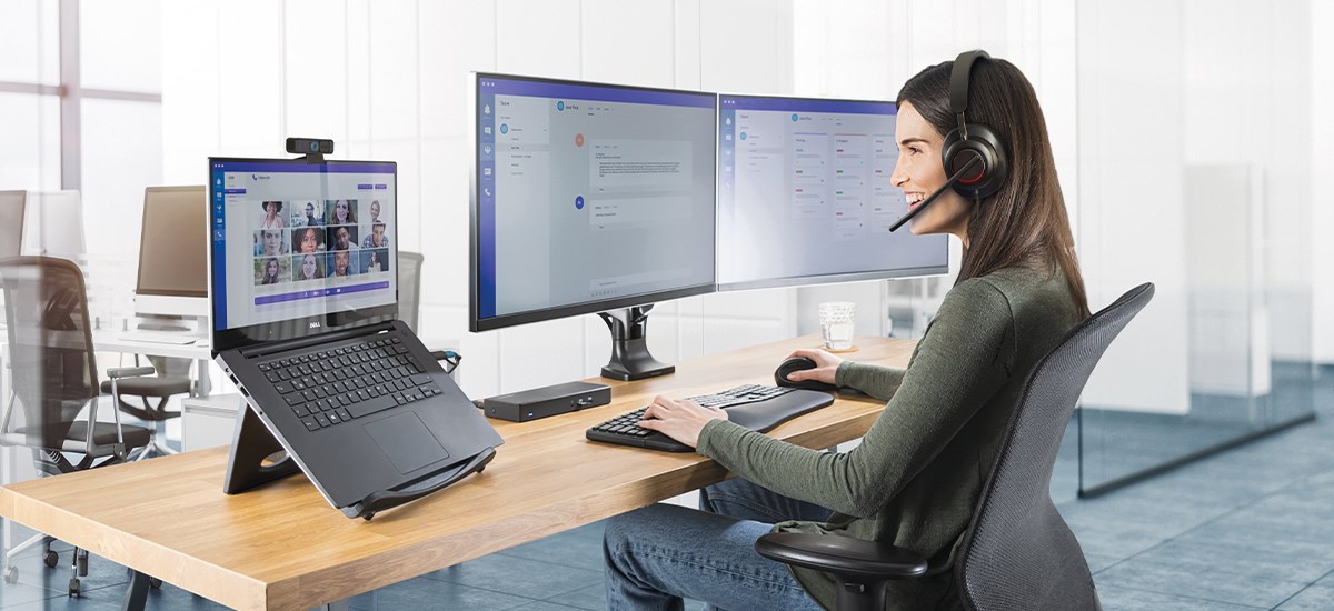 Woman working in her office at a wooden desk with a laptop on a Kensington laptop riser. 