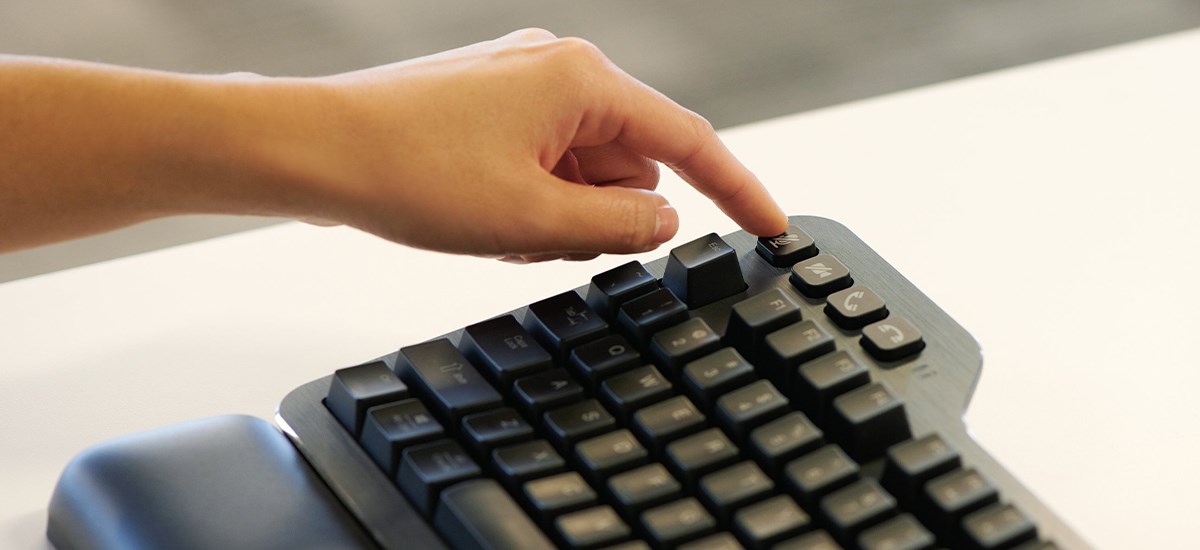 A hand muting a video call through the buttons of the Kensington silent mechanical Keyboard.
