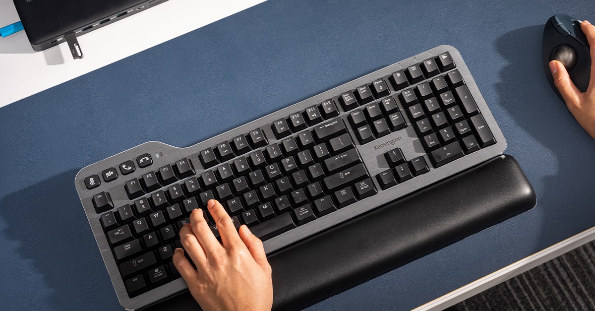 Kensington mechanical keyboard on a desk with a wrist rest and hands handling a trackball.