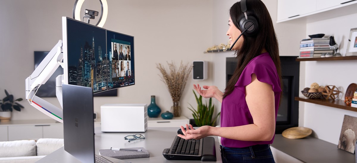 Woman having a video call with Kensington's professional video conferencing equipment and the new MK7500F QuietType™ Mechanical Keyboard on her desk. 