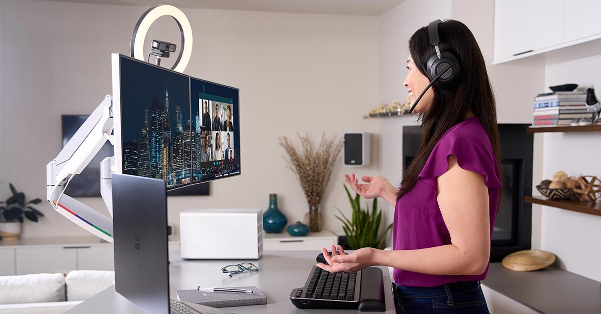 Women talking on a headset in a virtual meeting with a desk setup featuring a Ring light, webcam and keyboard.