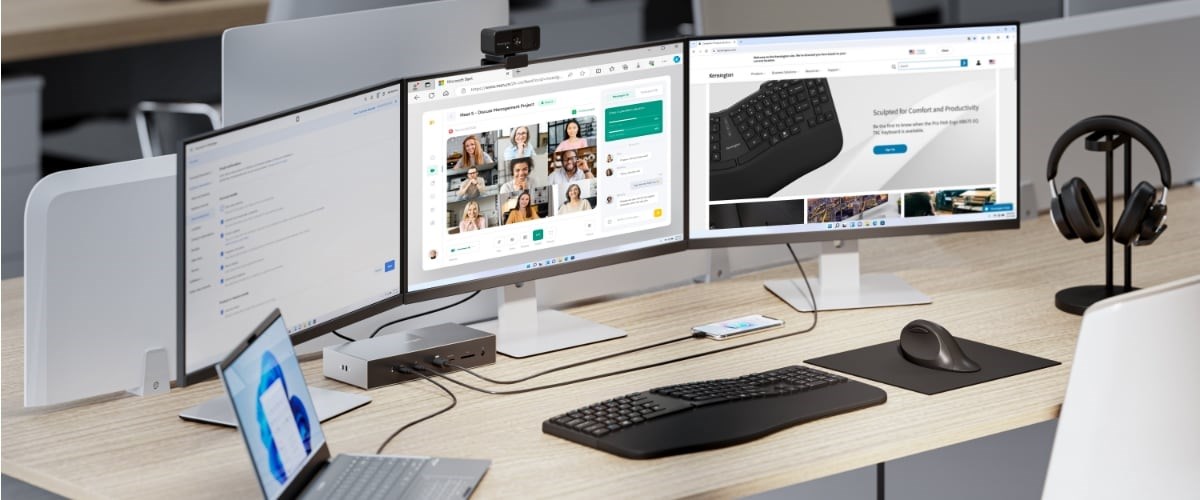  Desk setup featuring a laptop, three monitors, a Kensington Thunderbolt™ docking station, a keyboard, mouse, smartphone, and headphones on a stand.