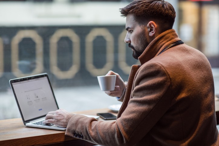 A young professional with a cup of coffee working on their laptop.