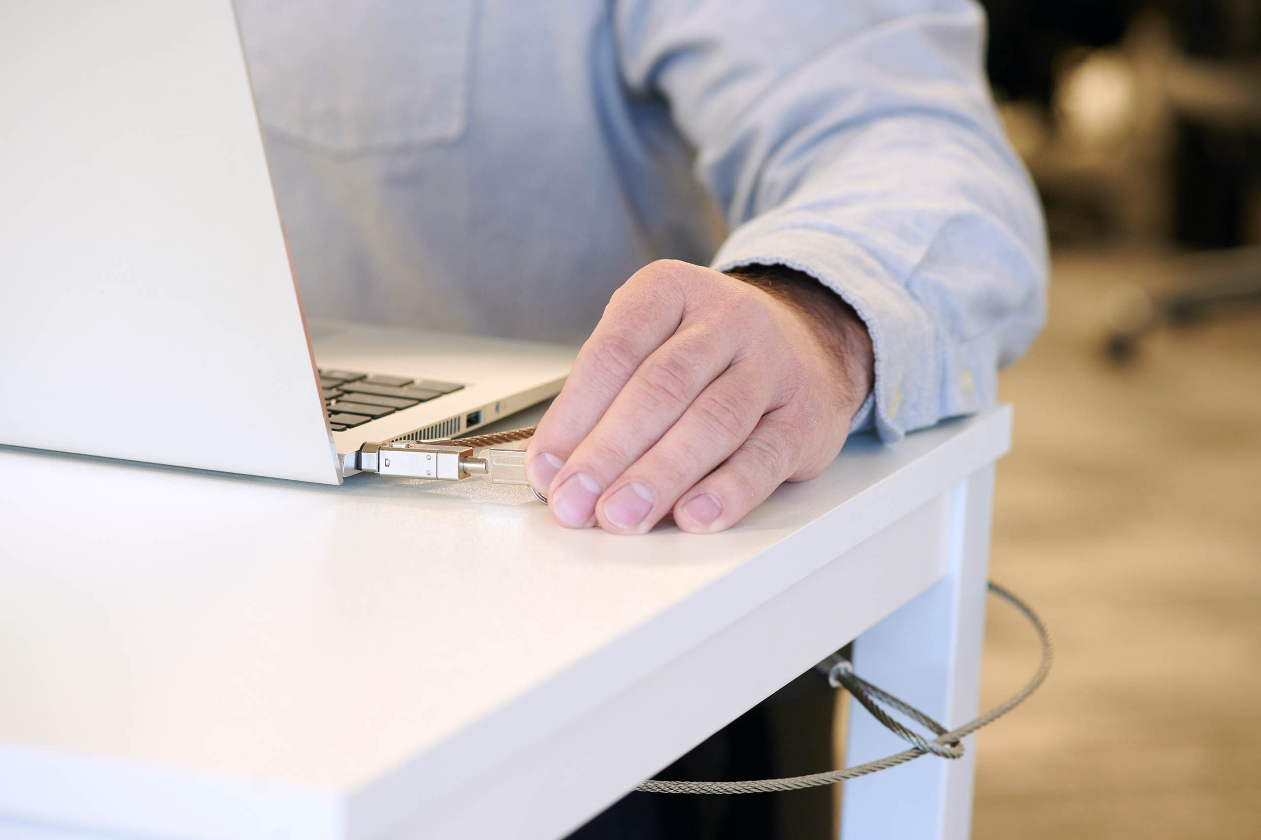 A person in a light blue long-sleeve shirt secures their laptop with a lock.