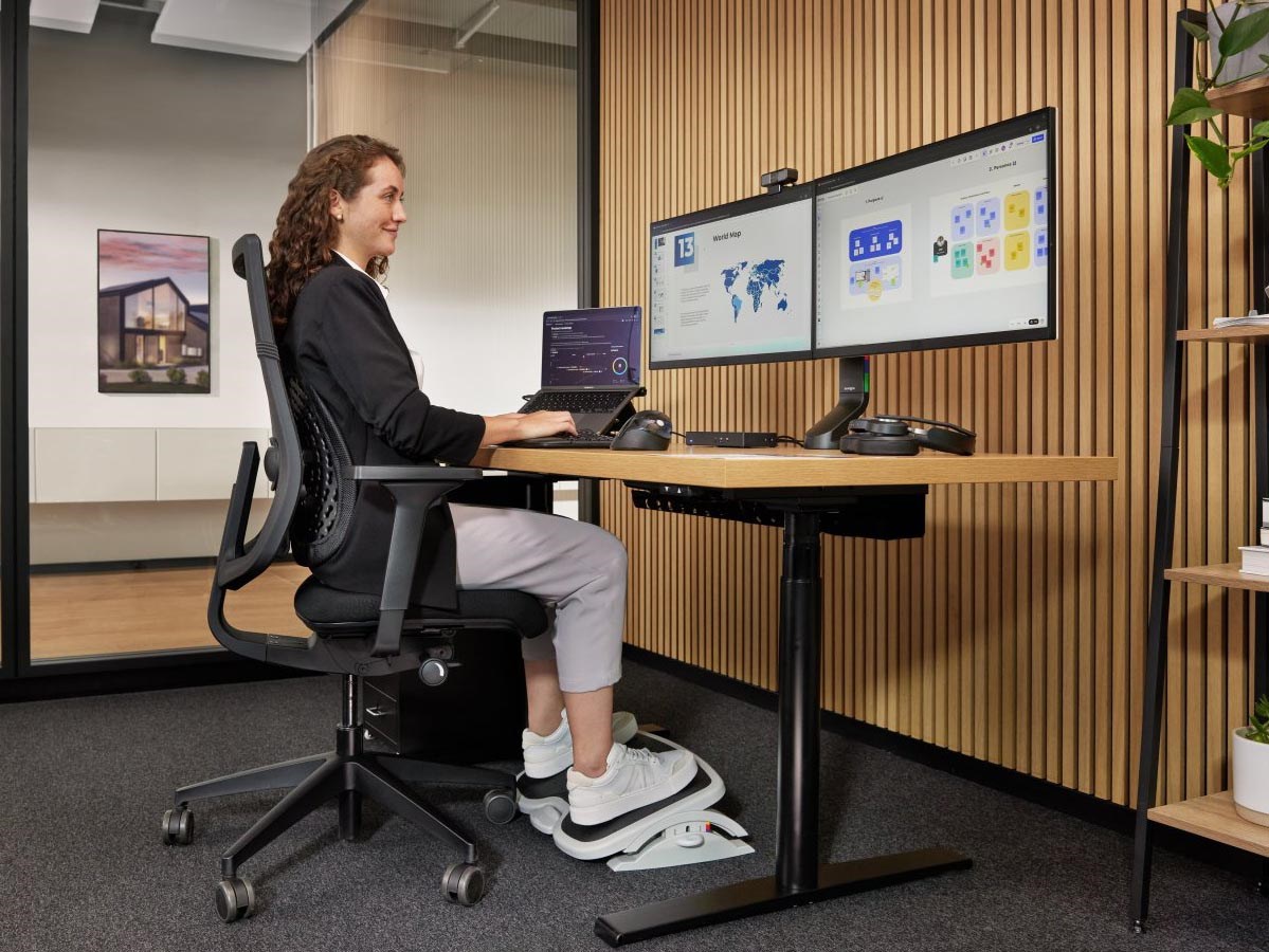 A professional working at the desk with two monitors and a laptop positioned on their eye level.