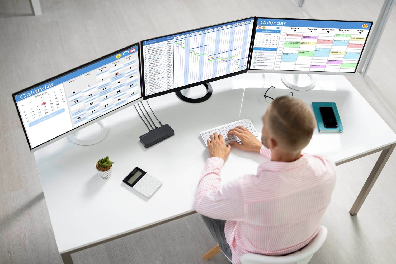 A professional working at the desk with three monitors connected to a docking station.