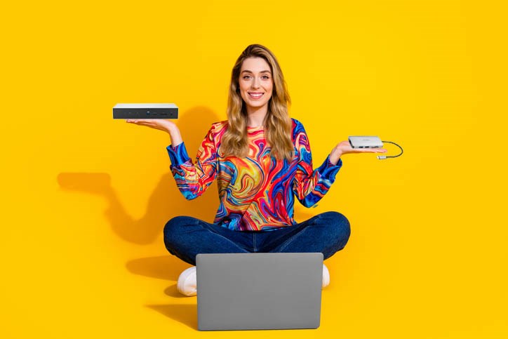 A person is sitting in front of their laptop, holding a docking station in one hand and a hub in the other.