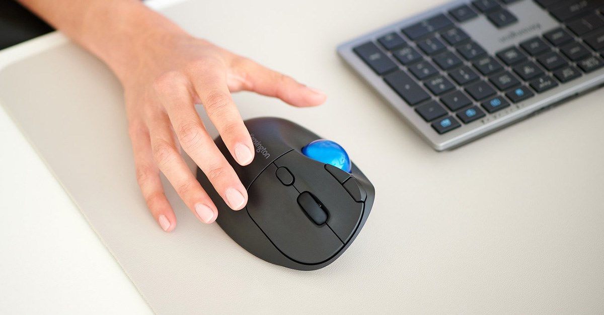 Close-up of a hand using a thumb-operated trackball mouse with a bright blue ball, placed next to a compact keyboard.