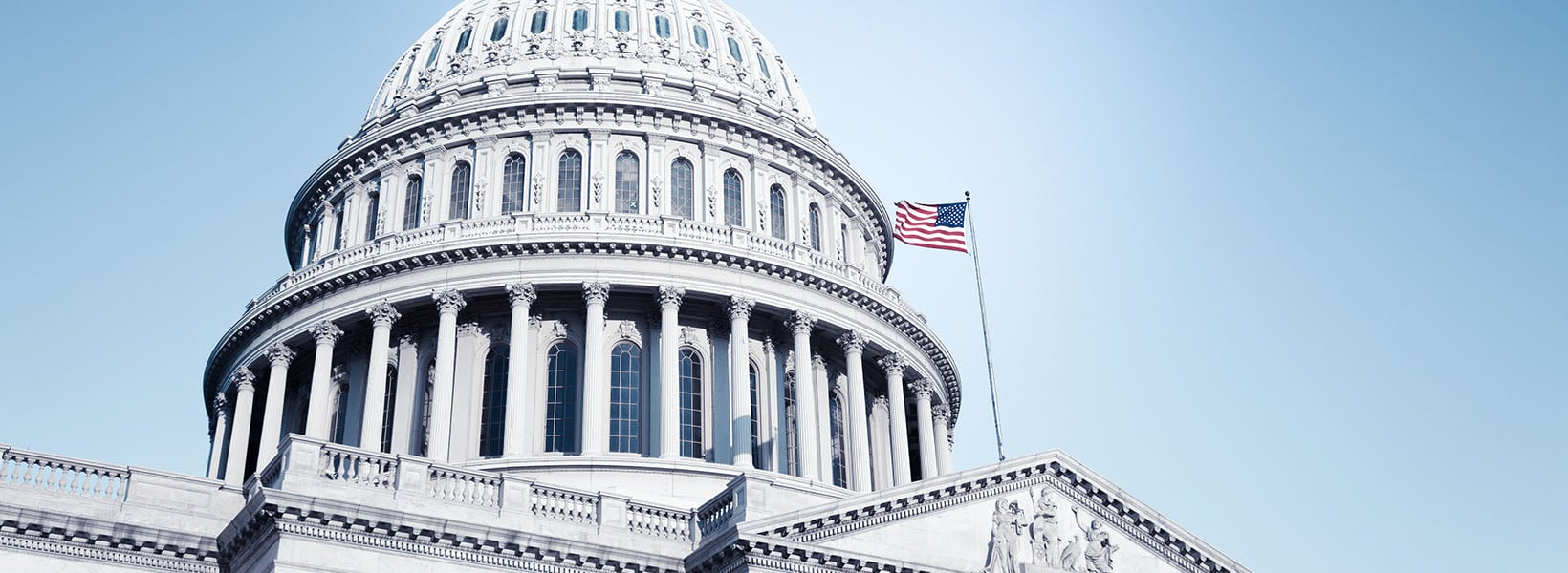 Close-up view of the U.S. Capitol dome with an American flag waving against a clear blue sky.