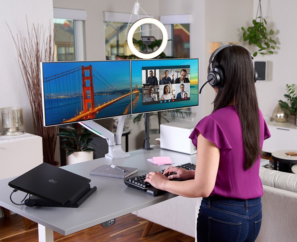 视频会议上配备 H3000 耳机、环形灯、三屏幕显示，并使用静音机械键盘的女士。