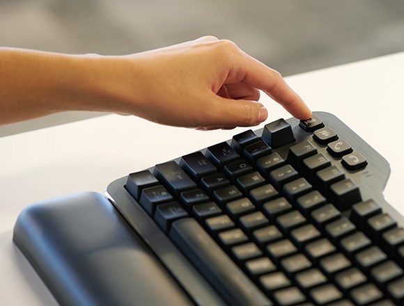 Person's finger pressing customizable meeting control buttons on Kensington's MK7500F Silent mechanical keyboard with wrist rest.