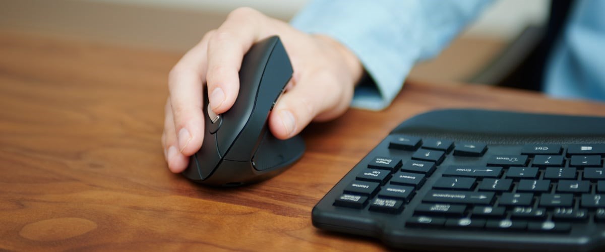 A man using a Kensington vertical mouse and keyboard on a desk.