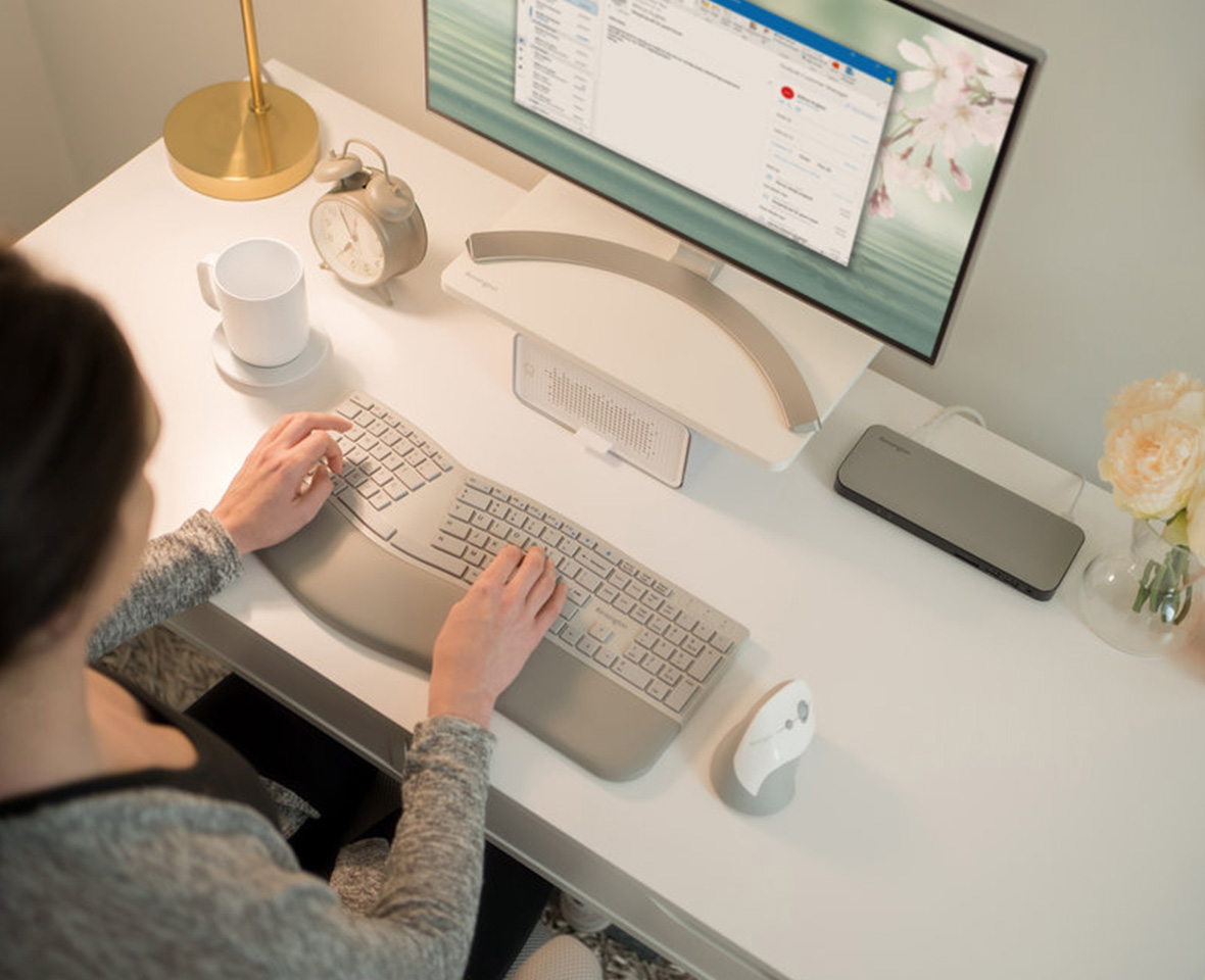Une femme à un bureau chez elle tapant sur un clavier ergonomique.