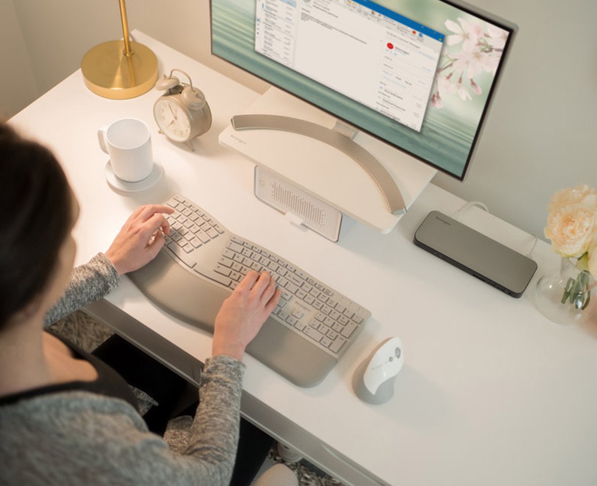 Mulher digitando no teclado ergonômico na mesa em casa.