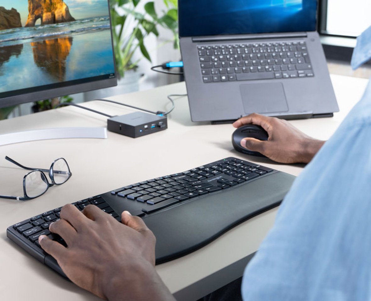 Uomo che scrive con la tastiera ergonomica e stringe un mouse verticale, seduta alla scrivania