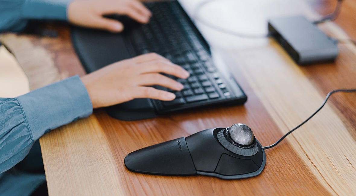 Mouse de trackball na órbita Kensington e pessoa digitando no teclado ao fundo